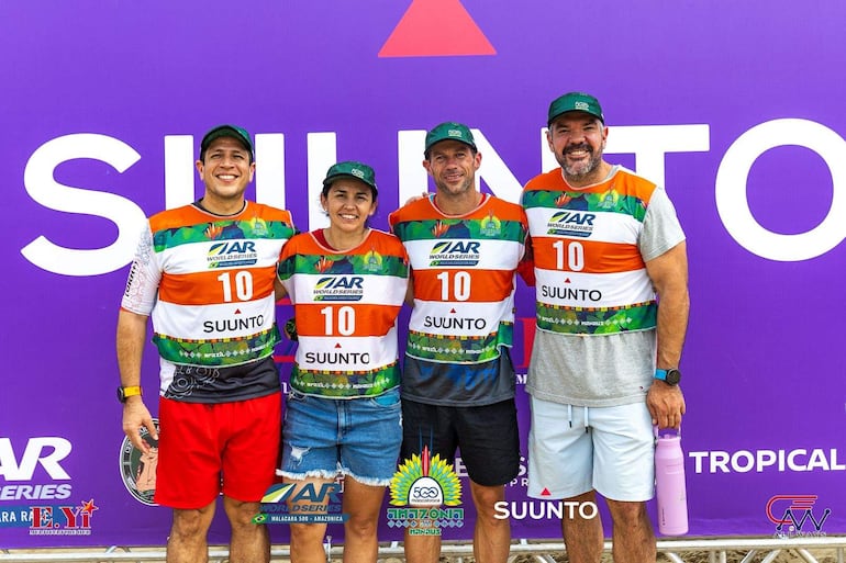 Cuatro personas, una mujer y tres hombres, sonríen con camisetas de colores brillantes y logo de SUUNTO, en un fondo morado.