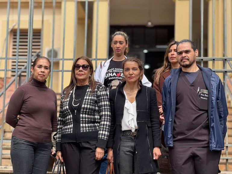 Rosanna González y Marlim Riveros Pesoa, vestidas formalmente, se ven serenas mientras posan ante un edificio.