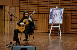 María Paz Cubells sentada en una silla, tocando guitarra acústica con cabello rizado y atuendo oscuro en un escenario profesional.