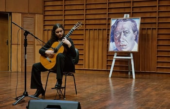 María Paz Cubells sentada en una silla, tocando guitarra acústica con cabello rizado y atuendo oscuro en un escenario profesional.