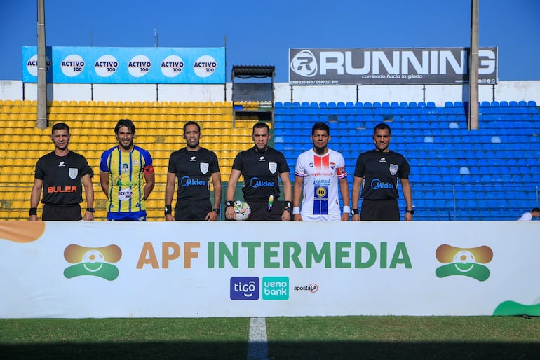 Jorge "El conejo" Benítez (izquierda) y Marcos Riveros, capitanes de ambos equipos, posan junto a la terna arbitral en Capiatá.