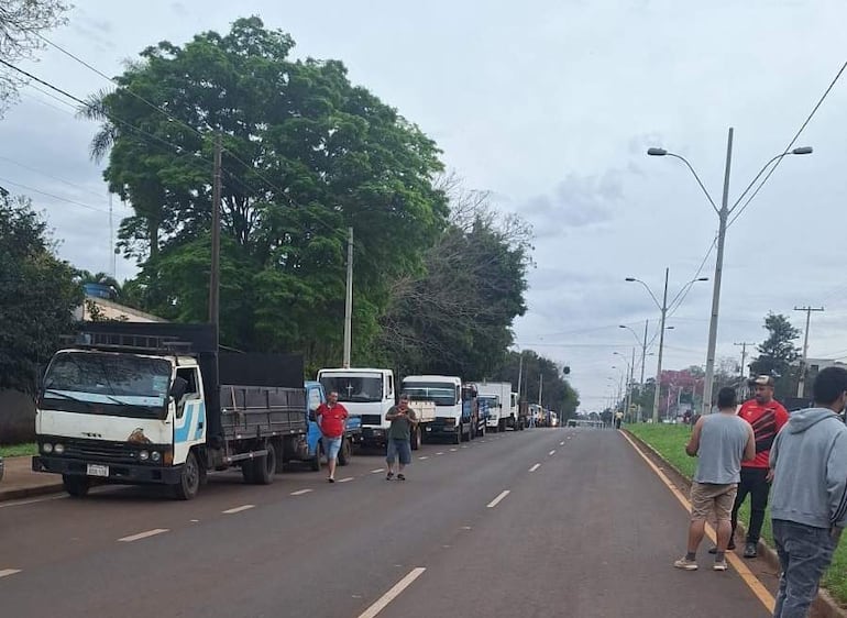 Grupo de camioneros discutiendo en la calle, algunos visten camisetas rojas y grises, bajo un cielo nublado.