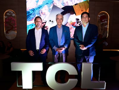 Tres hombres de pie: uno en camisa blanca y saco a cuadros, otro en camisa azul clara, y el tercero en camisa azul oscuro, en evento de TCL.