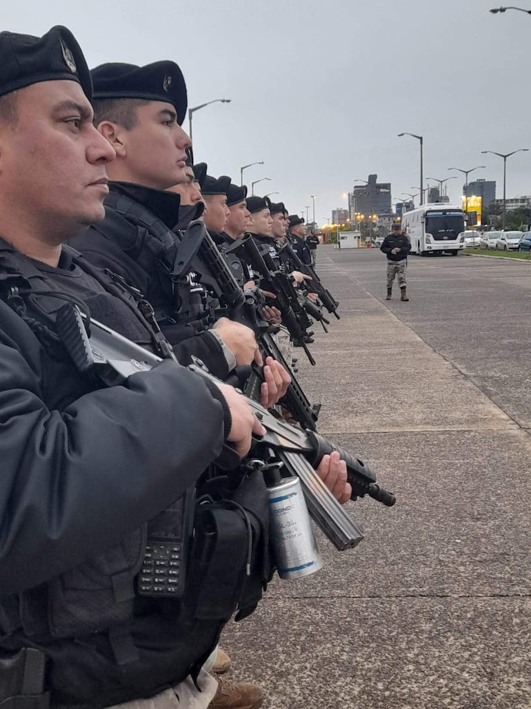 Grupo de policías en formación con uniformes oscuros y armas largas, alineados en el estacionamiento de Playa San José.