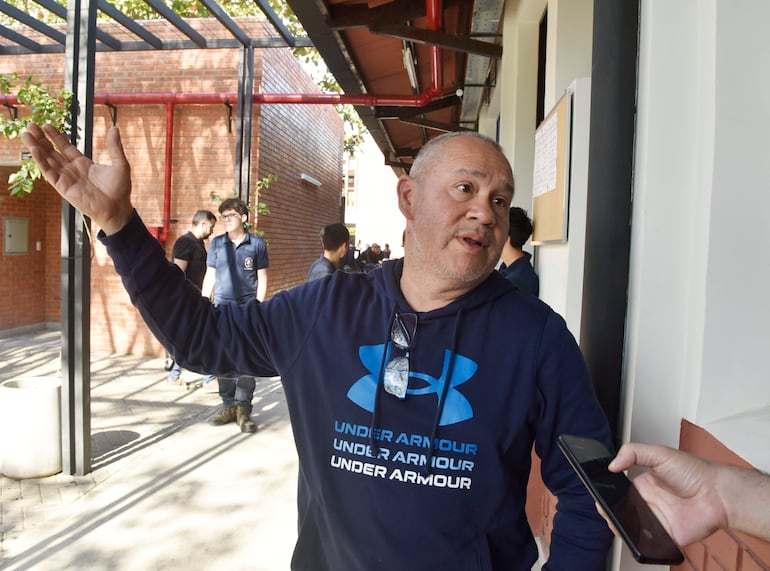 Hombre de cabello canoso en chaqueta azul oscuro gesticula mientras conversa con un grupo.