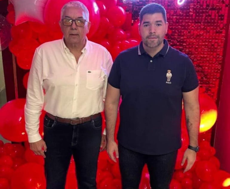 Juan Alberto Radice en camisa blanca y pantalones oscuros, junto a su hijo Jorge con camiseta negra, rodeados de globos rojos.