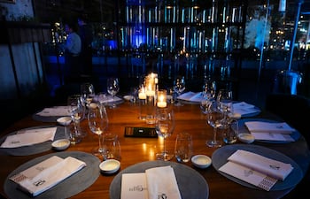 Mesa circular elegante con manteles neutros, velas encendidas, copas de vino y platos en un ambiente acogedor.