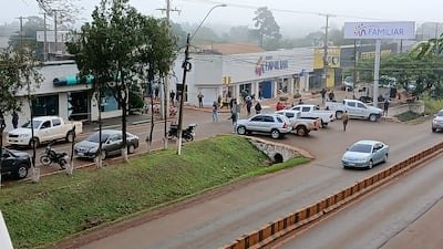 Grupo de personas en la acera, observando la situación, con vehículos en movimiento y un banco cercano.