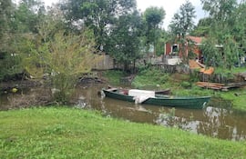 Embarcación de madera verde amarrada cerca de un estante rodeado de vegetación en un ambiente nublado.