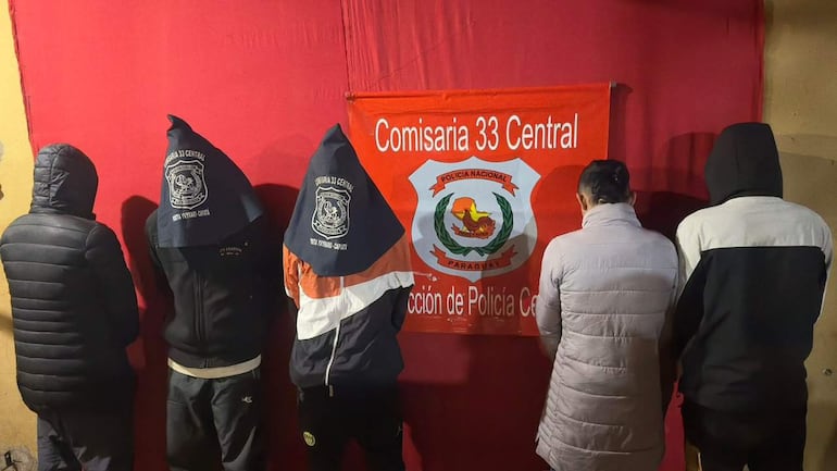 Cinco personas de espaldas, vestidas con chaquetas y capuchas, en la Comisaría 33 Central de Paraguay.