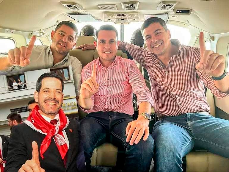 Pedro Alliana y Santiago Peña sonríen en un interior de avión, ambos con ropa a rayas y mostrando el número uno con sus manos.