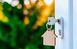 Cerradura de puerta con llave insertada y llavero en forma de casa con fondo de vegetación desenfocada.