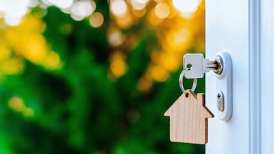 Cerradura de puerta con llave insertada y llavero en forma de casa con fondo de vegetación desenfocada.