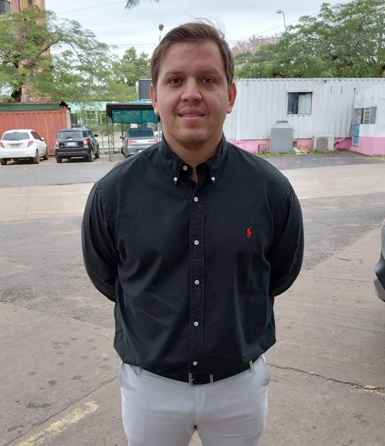 Rodrigo Delvalle de pie, con camisa negra y pantalones claros, en entorno urbano con coches estacionados y construcción cercana.