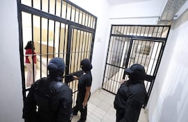 Tres hombres encapuchados en el interior de una celda, donde Dalia López, vestida con camiseta roja, conversa atentamente.