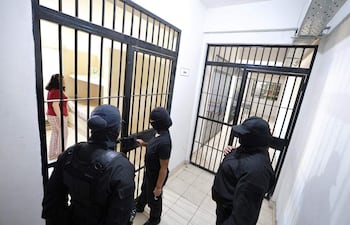 Tres hombres encapuchados en el interior de una celda, donde Dalia López, vestida con camiseta roja, conversa atentamente.