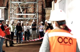 Varios trabajadores con cascos prestan atención a un guía en la restauración de un histórico templo, rodeados de andamios.