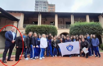 Instructor robusto con traje oscuro y gafas al frente, rodeado de niños y adolescentes vestidos con ropa deportiva en un entorno amigable.