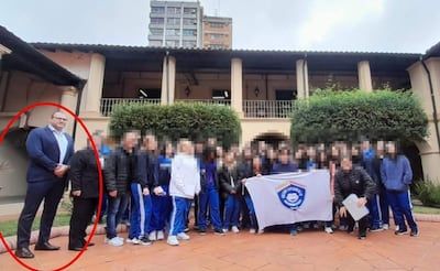 Instructor robusto con traje oscuro y gafas al frente, rodeado de niños y adolescentes vestidos con ropa deportiva en un entorno amigable.