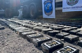 Paquetes rectangulares de cocaína en el suelo, con agentes de policía supervisando la incautación en un entorno de operaciones.