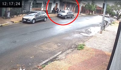 Dos personas de espaldas frente a un local, con cielo nublado y charcos en la calle tras haber llovido.
