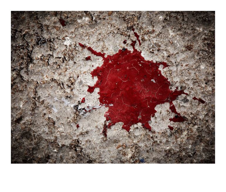 Superficie de concreto desgastado con mancha roja irregular, evocando emociones en un ambiente urbano.