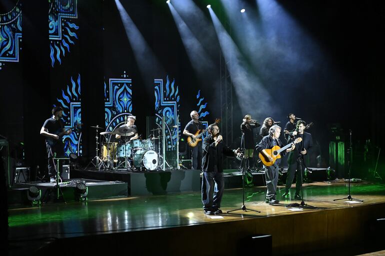 Ocho músicos en el escenario, con guitarras y baterías, iluminados por luces brillantes durante el concierto de Los Nocheros.