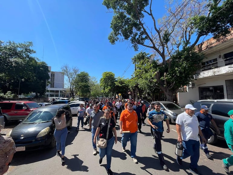 Grupo de personas marchando en la calle, vistiendo ropa casual y expresiones de felicidad en un día soleado.