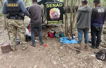 Agente de la SENAD con chaleco identifica a un hombre con camisa gris y jeans oscuros, rodeados de un ambiente natural.
