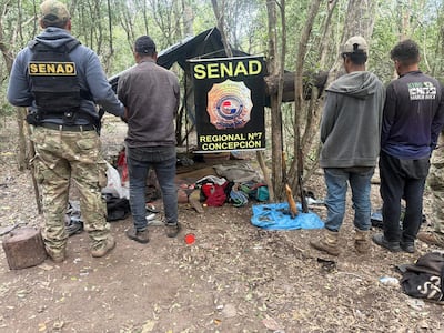 Agente de la SENAD con chaleco identifica a un hombre con camisa gris y jeans oscuros, rodeados de un ambiente natural.