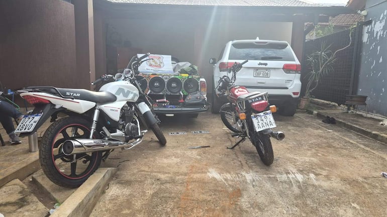 Garaje con dos motocicletas, una blanca y negra y una roja, junto a un SUV blanco con matrícula visible.