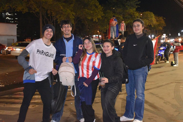 Grupo de seis personas sonrientes en un automóvil, luciendo gorras y camisetas con colores nacionales de Paraguay, en un ambiente festivo nocturno.