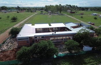Edificio de múltiples niveles en construcción, rodeado de naturaleza y materiales apilados en un ambiente rural.