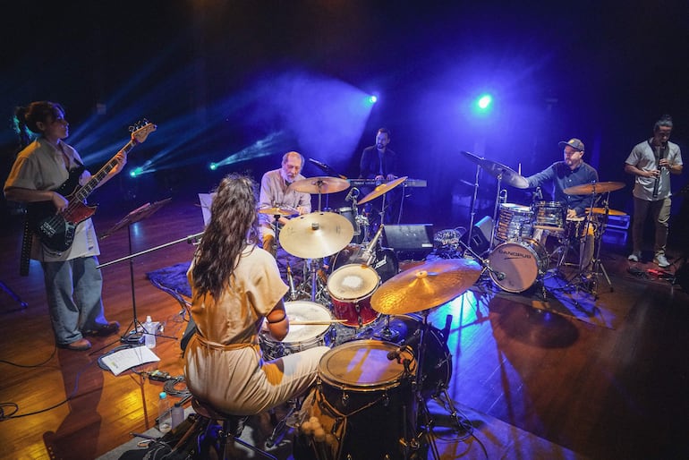 Toti, Víctor y Julieta Morel en concierto, tocando enérgicamente rodeados de luces azules y moradas.