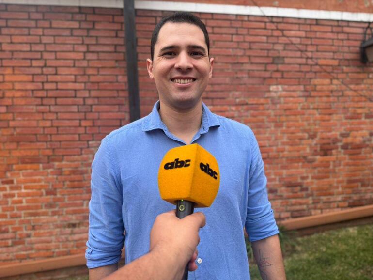 Pablo Callizo sonríe mientras sostiene un micrófono, con una pared de ladrillos como fondo.