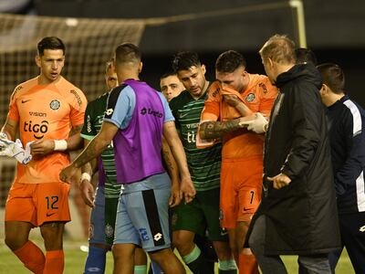 El uruguayo Gastón Olveira (derecha de naranja), jugador de Olimpia, es asistido y retirado del campo de juego después de sufrir una lesión en el brazo derecho en el partido contra Resistencia por la segunda fecha del torneo Clausura 2023 del fútbol paraguayo en el estadio Antonio Aranda Encina, en Ciudad del Este.