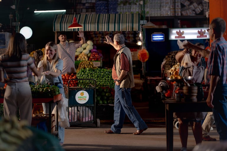 Mujeres y hombres alegres conversan en el mercado ABASTO NORTE, con productos expuestos y luces cálidas.