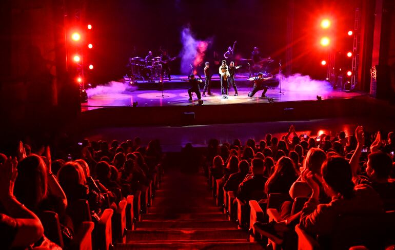 Cantante con micrófono en el centro del escenario, rodeada de bailarines y un público emocionado que aplaude.