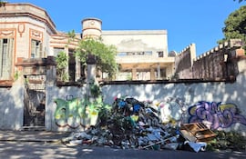 Edificio antiguo con ornamentación en la fachada, rodeado de basura y grafitis en un entorno urbano descuidado.