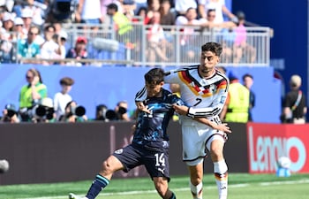 Andrés Cubas en camiseta oscura intenta patear el balón mientras un jugador alemán con camiseta blanca lo sostiene, rodeados de espectadores.