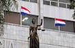 Escultura femenina de la Justicia sosteniendo balanzas, con banderas de Paraguay ondeando en el fondo.