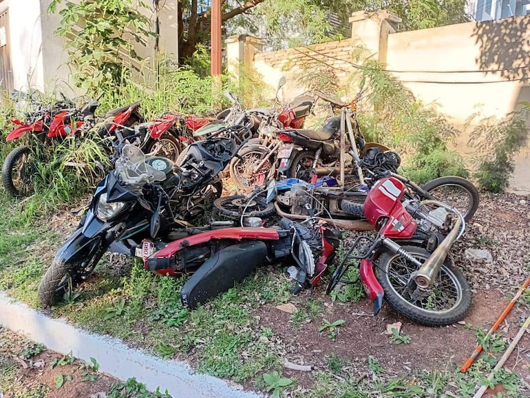 Motocicletas apiladas en un terreno con maleza, reflejando deterioro y abandono en un ambiente descuidado.