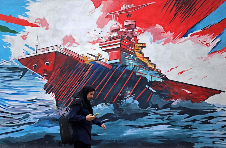 Una mujer camina frente a un mural alegórico a la crisis en Ormuz, en Teherán, Irán.