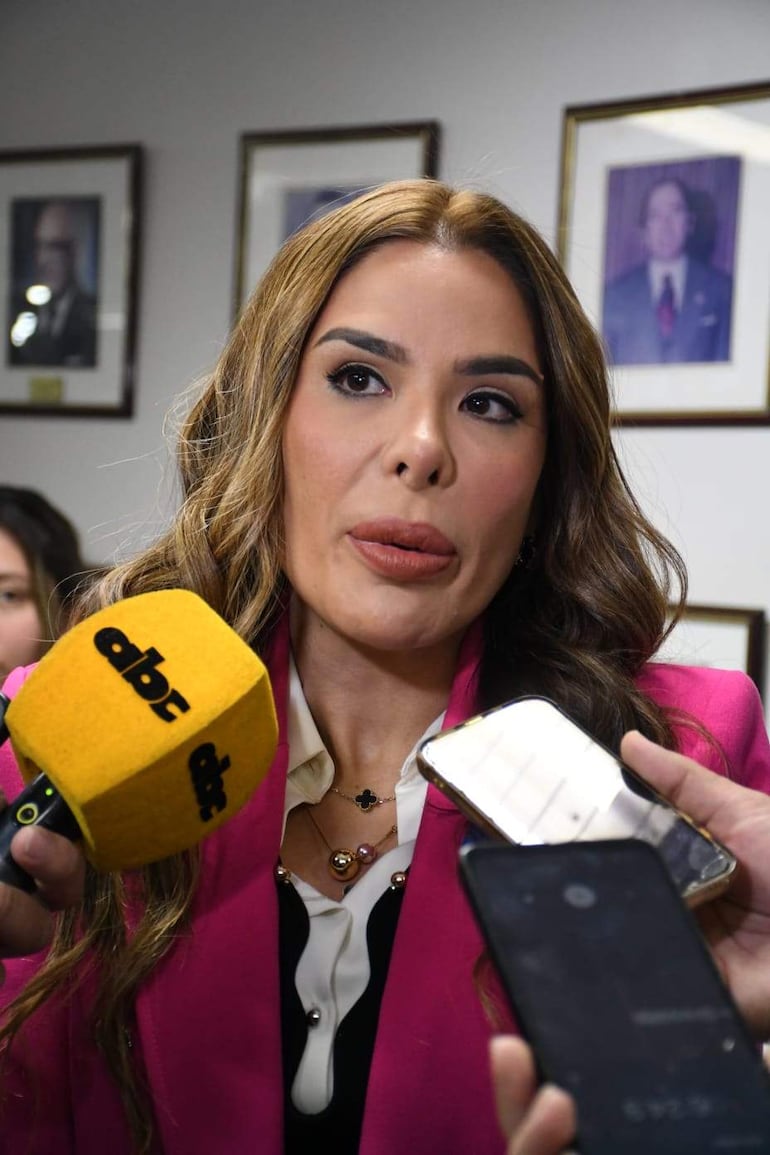 Fiorella Forestieri en blazer rosa y blusa blanca, rodeada de periodistas con micrófonos en un entorno institucional.