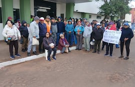 Grupo de adultos mayores en San Ignacio, con mujer al frente sosteniendo cartel sobre pensión universal, vestidos abrigados y serios.