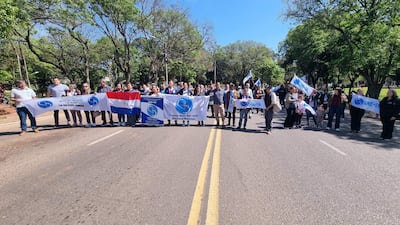 Grupo de manifestantes sosteniendo pancartas, con camisetas claras, en un entorno verde y cielo despejado durante la protesta.