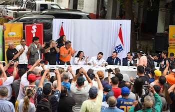 Luis Bello y Jorge Sabate aplauden mientras firmantes en mesa central celebran el contrato colectivo rodeados de banderas paraguayas.