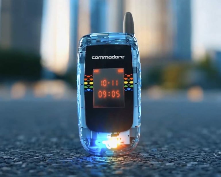 Teléfono móvil retro de Commodore sobre superficie asfáltica, con pantalla iluminada en color naranja que muestra la hora.