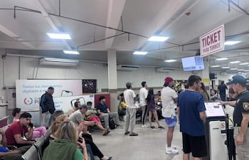 Varias personas en espera en interior de oficinas, algunos sentados y otros de pie, con un funcionario asistiendo a un joven.