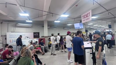 Varias personas en espera en interior de oficinas, algunos sentados y otros de pie, con un funcionario asistiendo a un joven.